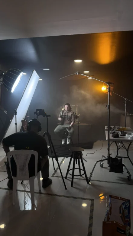 Iván De León, saxofonista profesional, en una sesión de fotos en estudio con un ambiente cinematográfico. Rodeado de equipo de grabación, luces de producción y una atmósfera con humo, se prepara para una sesión visual impactante. La imagen captura el proceso creativo y la producción de contenido musical profesional.